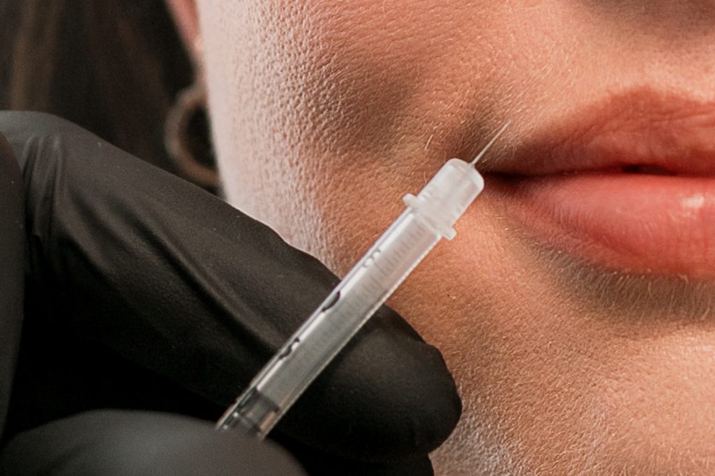 Nahaufnahme einer Hand mit Spritze, die sich nah an den Lippen einer Person befindet.